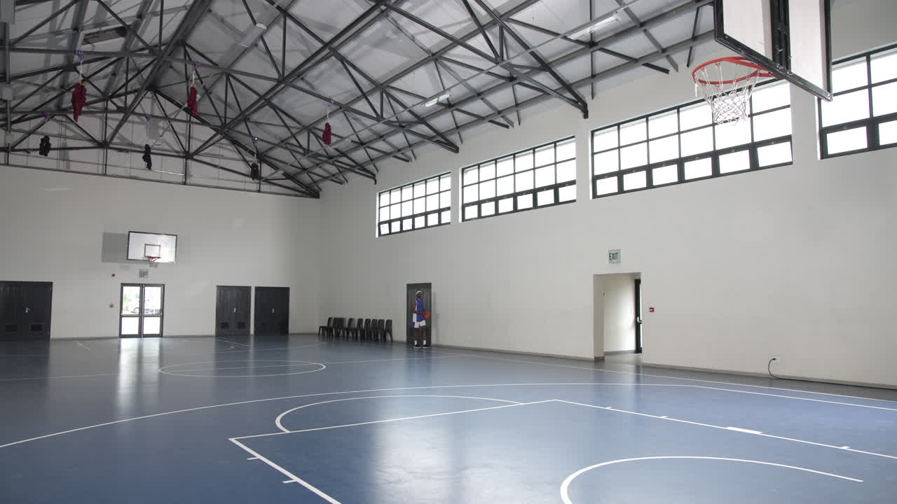 Basketball player practicing alone in spacious indoor gym, focusing on skills