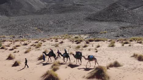 Caravana-De-Personas-Y-Camellos-O-Dromedarios-En-Fila-En-El-Desierto-De-Marruecos