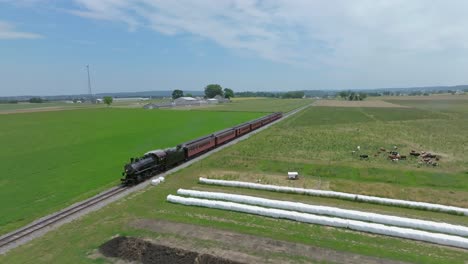 a steam passenger train travels through wide-open fields and rolling landscapes, showcasing vibrant green pastures and distant hills on a sunny day, perfect for train enthusiasts