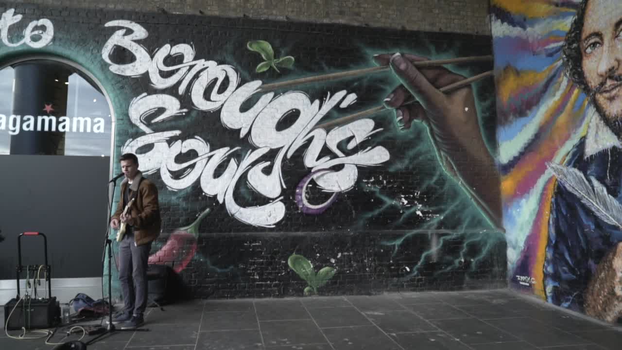 Musicista di strada davanti a un murale di graffiti raffigurante Shakespeare