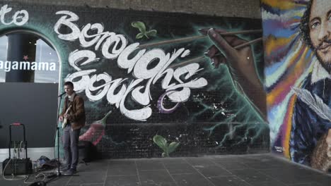 street musician in front of graffiti mural featuring shakespeare