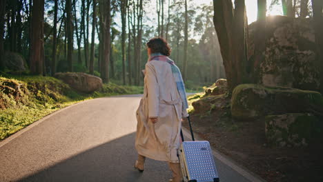 traveler walking forest road with suitcase illuminated bright autumn sunlight.