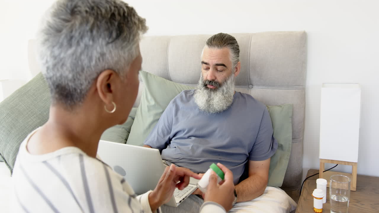 Discussing medication, senior couple using laptop in bedroom