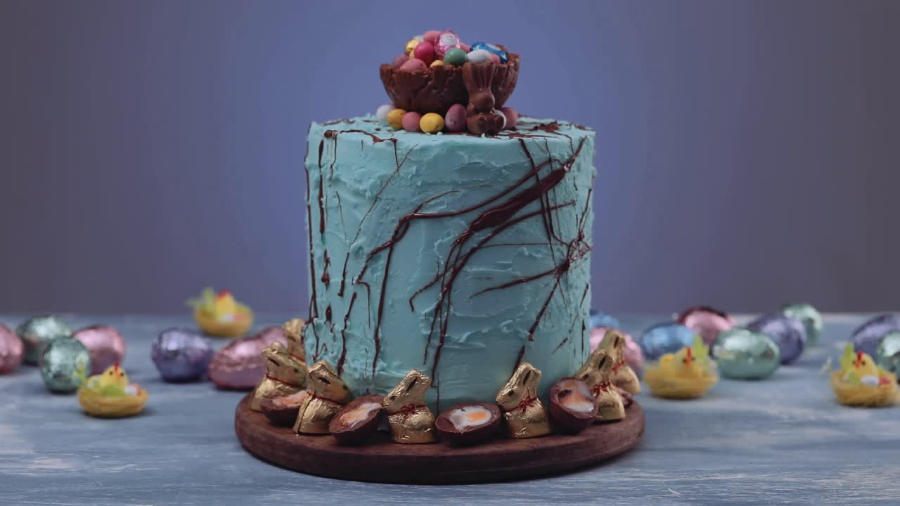 trato tradicional de pascua: delicioso pastel de nido de pascua azul decorado con conejos dorados y rodeado de huevos de pascua de colores sobre una mesa azul