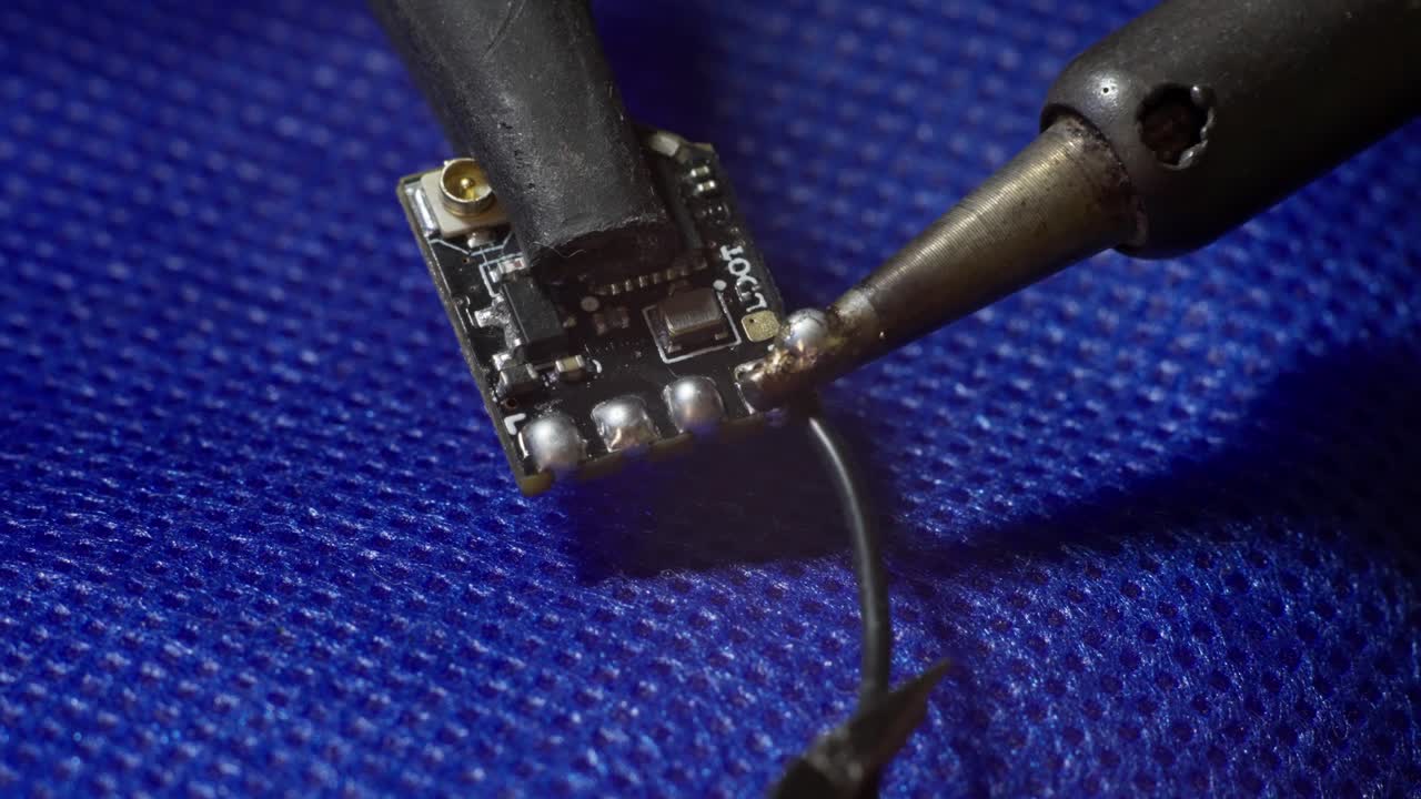 SLOW MOTION CLOSE UP SHOT OF A MAN CHIP SOLDERING A BLACK CABLE TO A MICRO CHIP
