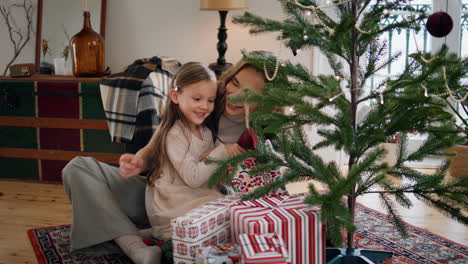 familia de navidad charla tierna cerca de árbol decorado en el interior. niña eligiendo regalo