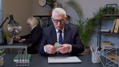 rich senior business manager counting money dollar cash after working on portable laptop at office