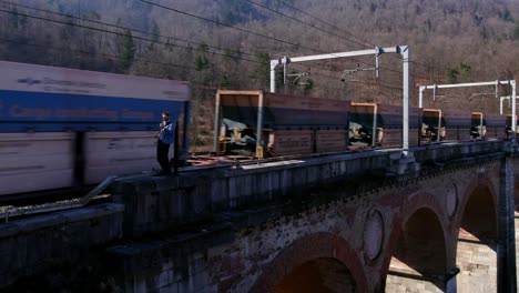 guitar player on a bridge with a moving train behind drone shot