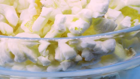 toma macro de palomitas de maíz en un recipiente de vidrio transparente girando sobre una superficie azul, vista de cerca en 4k