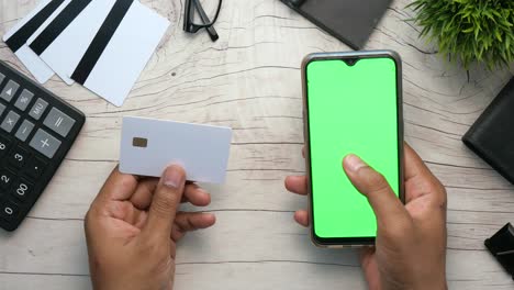 persona con una tarjeta de crédito y un teléfono inteligente con una pantalla verde
