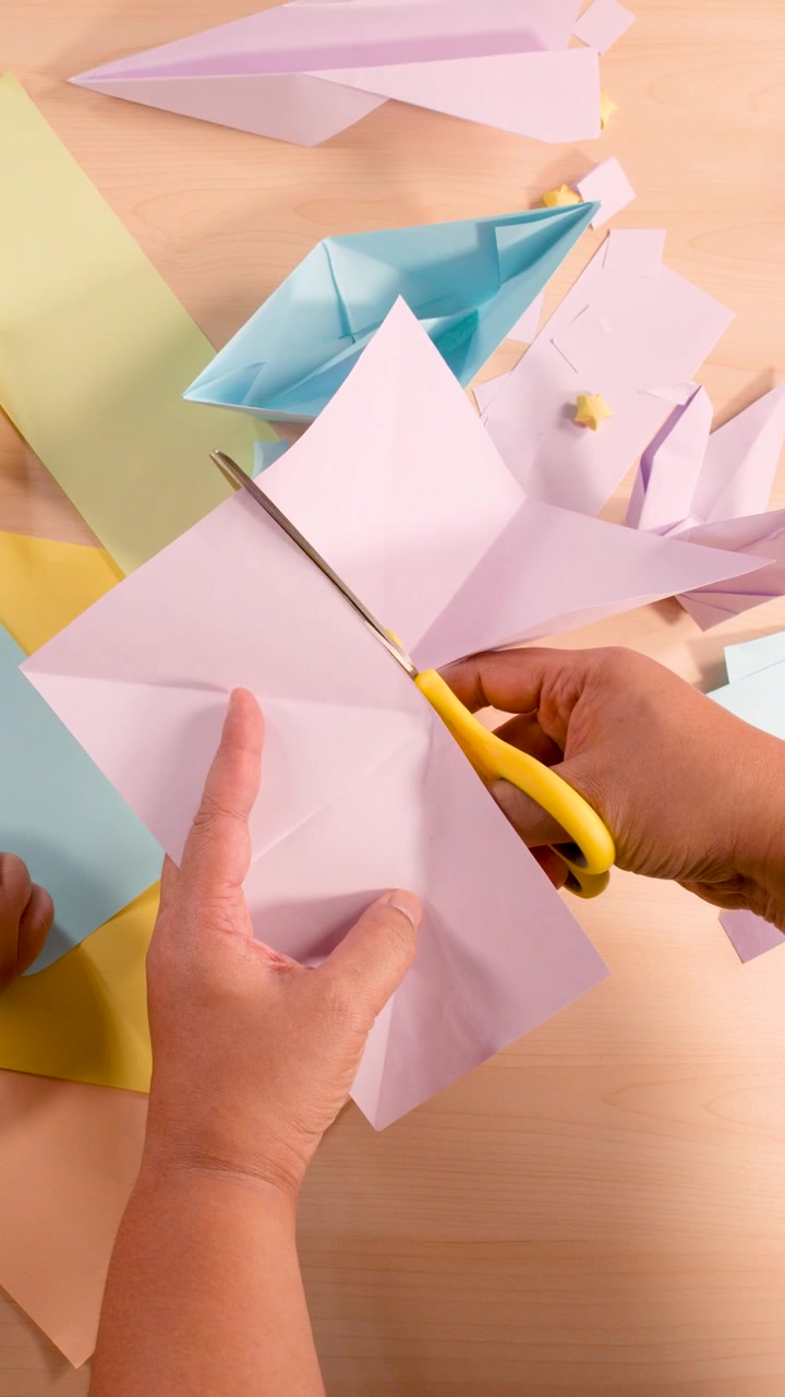Mani adulte tagliano carta pastello con le forbici, preparando forme di origami su un tavolo ben illuminato