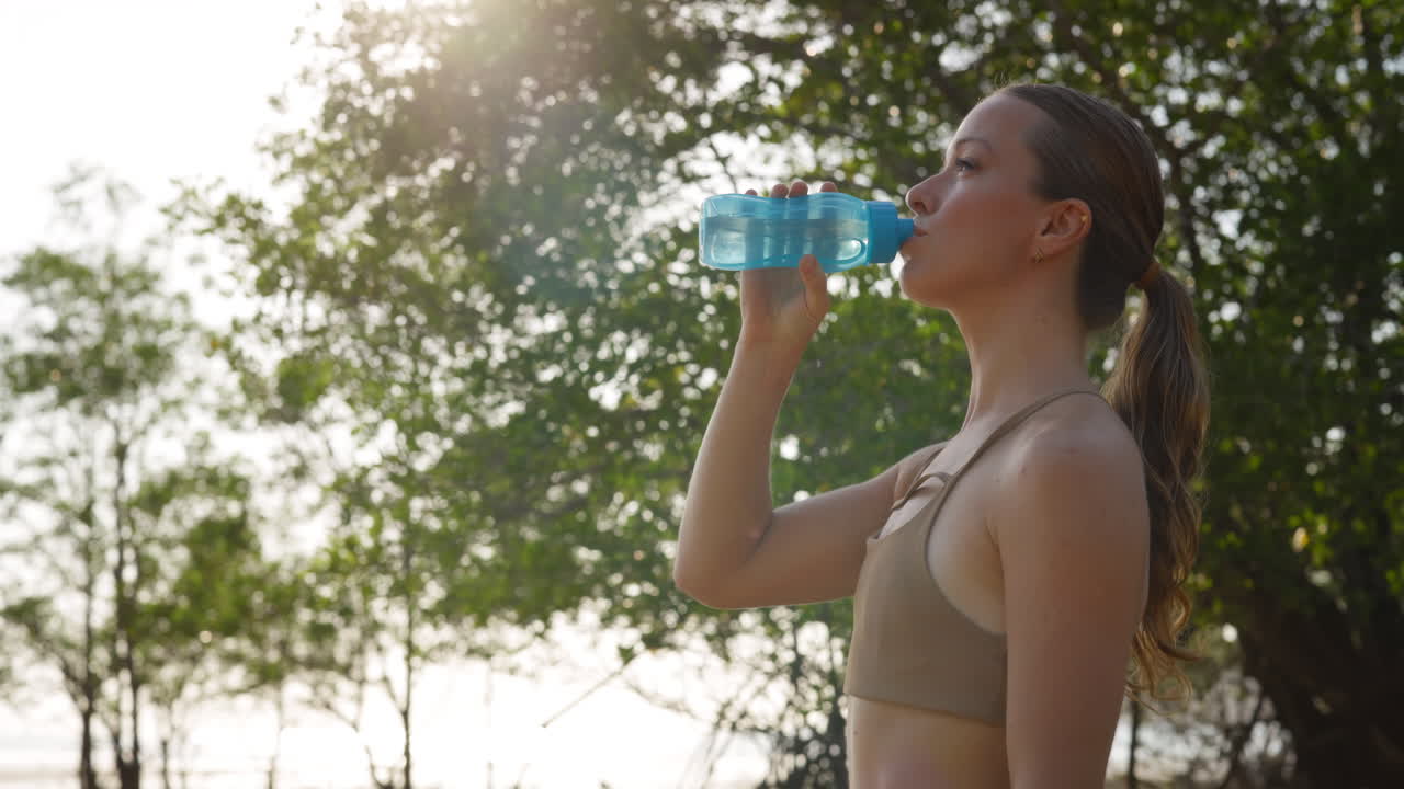 Giovane donna che beve acqua da una bottiglia all'aperto