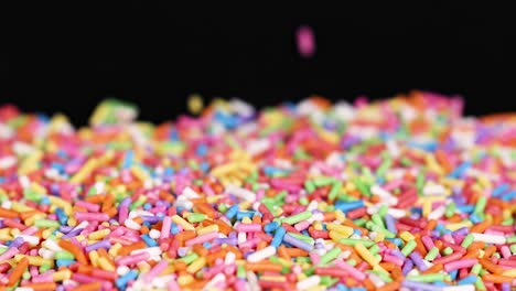 a colorful array of sprinkles accumulates on a dark background, creating a lively and textured scene.