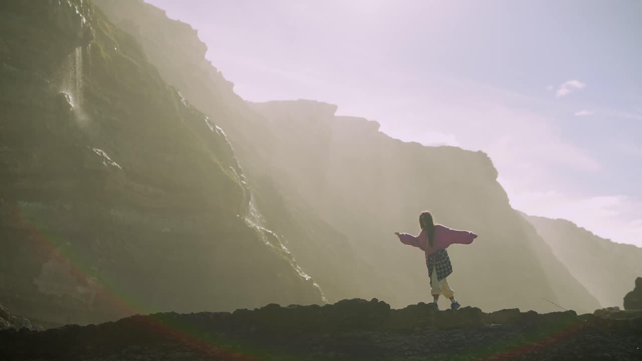 Young Woman Explores Misty Cliffs with Waterfalls and Sunlight