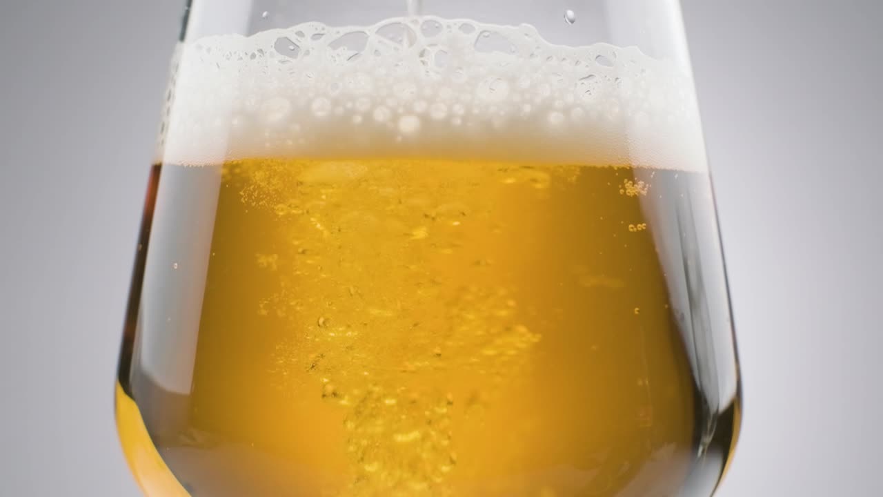cámara lenta, primer plano cerveza fresca vertida en vidrio, fondo blanco