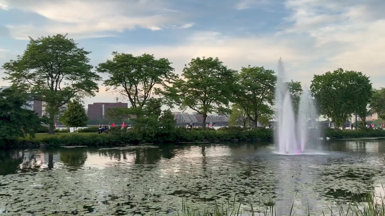 Fuente de parque urbano en la Explanada del Río Charles en la ciudad de Boston. Atardecer con sol bajo durante el verano y cielos parcialmente nublados.