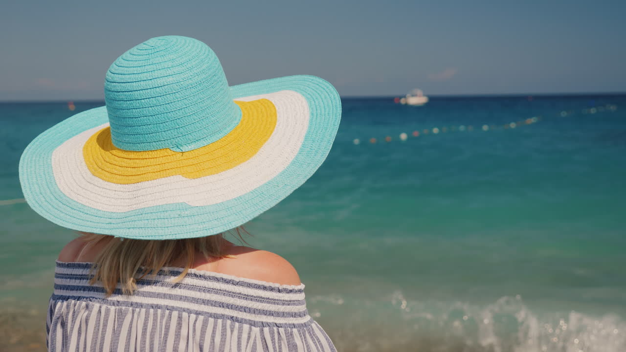 뒤에서 해변의 전망을 즐기는 밝은 꽃의 넓은 모자를 쓴 어린 소녀