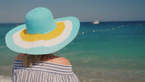 A-Young-Girl-In-A-Broad-Hat-Of-Bright-Flowers-Enjoying-The-Sea-View-On-The-Beach-View-From-The-Back