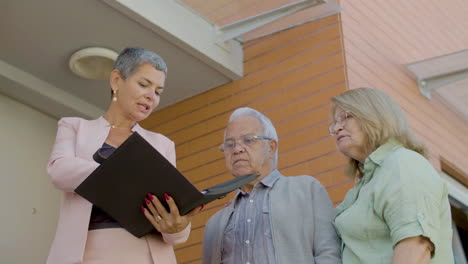 agente de bienes raíces sosteniendo un archivo y discutiendo los detalles de la venta con una pareja mayor