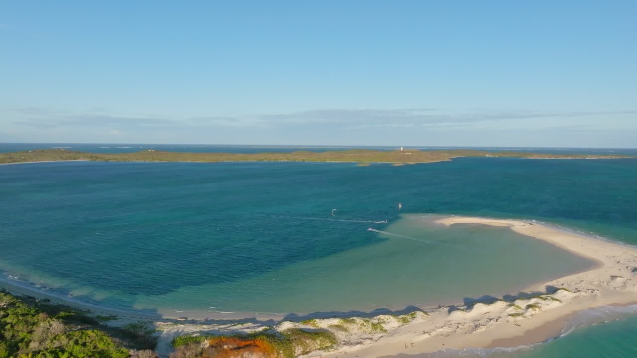 Drone performs an orbiting shot around a kitesurfer gliding along turquoise waters near a secluded island