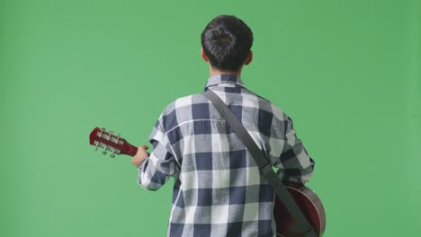 back view of young asian teen boy playing guitar and singing on the green screen background