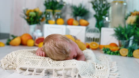 adorable blond infant trying to raise his head from the knitted pillow. cute blue-eyed baby boy in studio. oranges at backdrop.