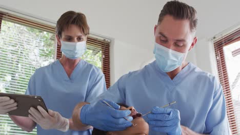 Caucasian-male-dentist-with-face-mask-examining-teeth-of-female-patient-at-modern-dental-clinic