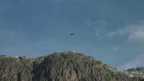 la silueta del avión no tripulado filma la cima de la montaña contra el cielo azul