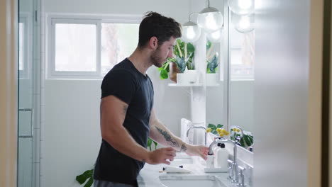 man wearing pyjamas standing at sink putting on moisturizer in bathroom