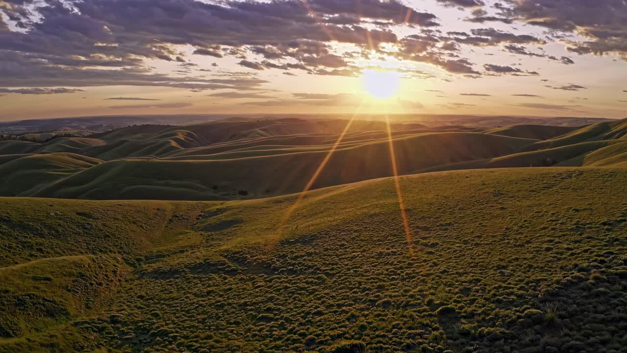 Aerial video captures a breathtaking sunset over rolling hills, with golden light casting long