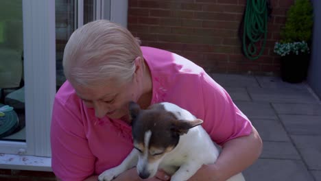 old woman talks to pet dog companion on her lap in garden