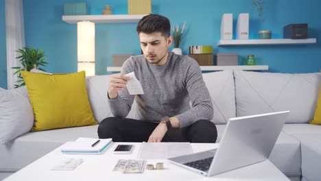 hombre frustrado mirando facturas haciendo cálculos con una calculadora en casa.