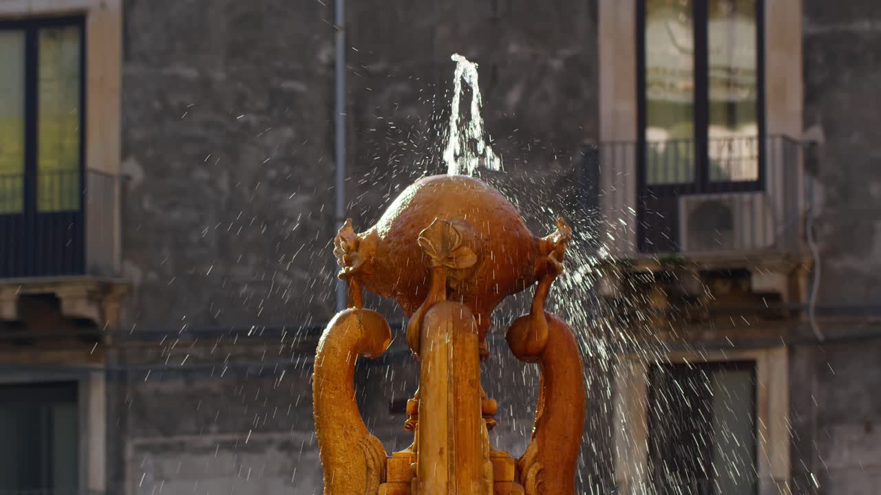 toma en cámara lenta de una fuente de agua con un edificio siciliano en el fondo, catania