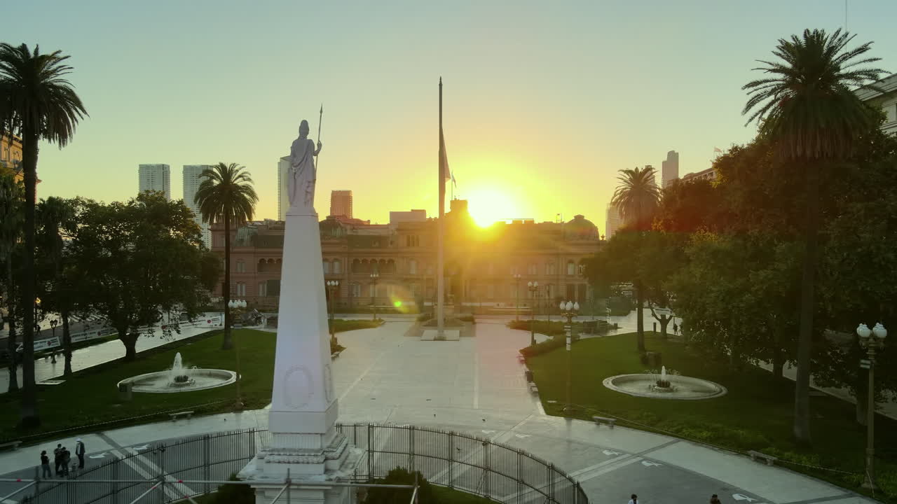 Aerial Drone Scene flying back of Casa Rosada, Buenos Aires, Argentina, the presidential pink house, May Pyramid. Warm dawn morning sun backlight, Pirámide de Mayo and flag. Flare, reflections.