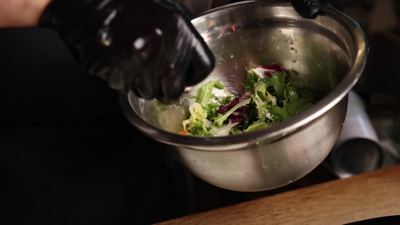 Chef's Hands in Gloves Preparing Fresh Salad in a Metal Bowl