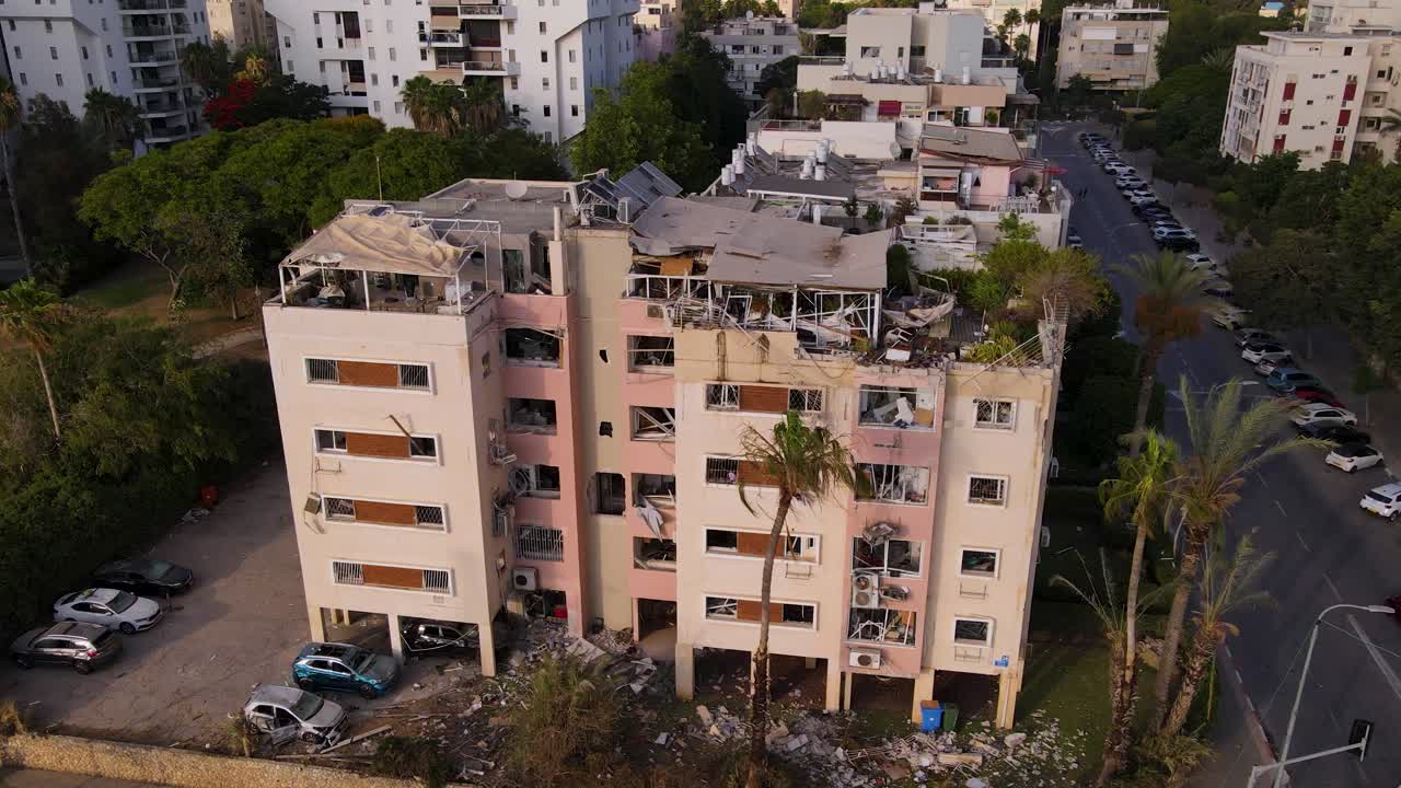 Drone circles a damaged building at Tel Aviv intersection with shattered interiors, parked cars, and scattered debris