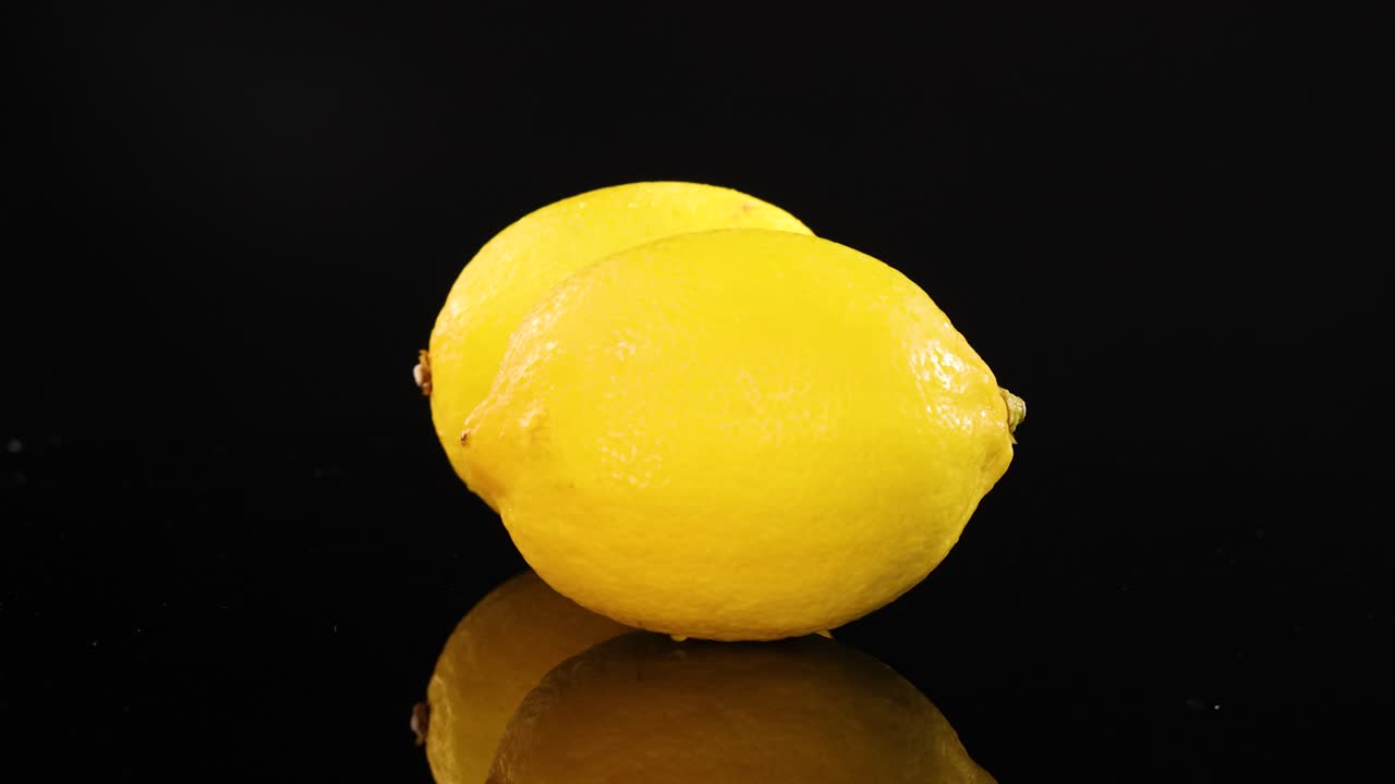 Two lemons rotate on a glossy black surface under bright lighting, creating a vibrant and dynamic visual effect