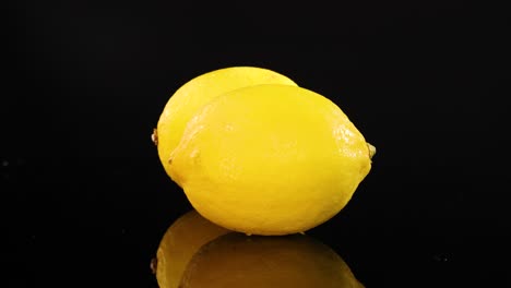 two lemons rotate on a glossy black surface under bright lighting, creating a vibrant and dynamic visual effect