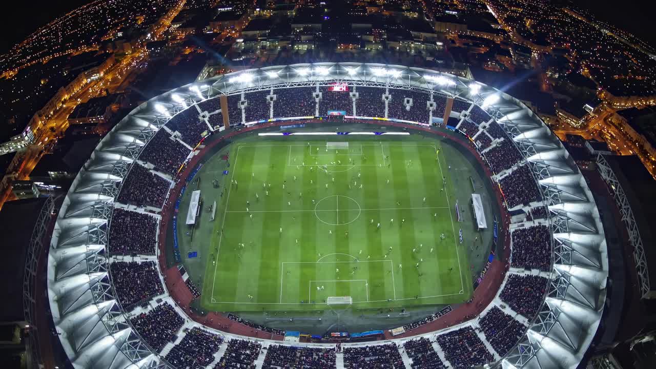 Vista aerea di uno stadio illuminato a giorno di notte, che riprende una partita di calcio