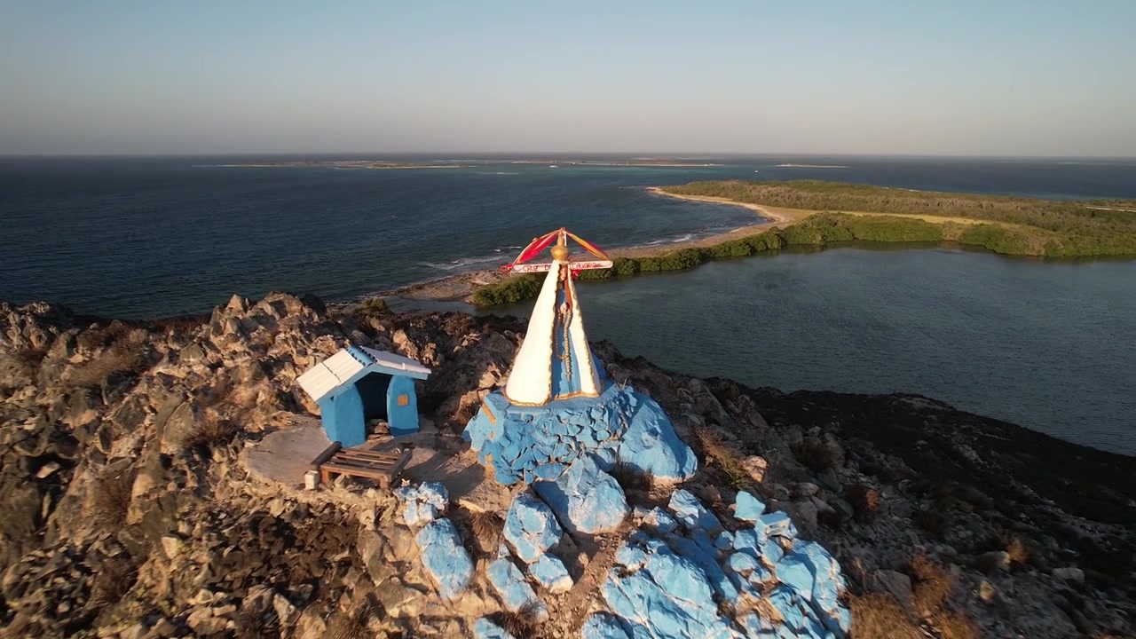 Impresionante toma aérea con dron capturando un colorido santuario religioso con la Virgen del Valle con vistas al tranquilo Mar Caribe durante la hora dorada en Los Roques
