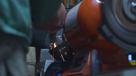 A-static-low-angle-shot-of-a-mechanic-polishing-a-welded-metallic-car-piece,-with-sparks-flying-down-his-spinning-polishing-wheel