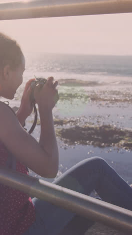 Animation-of-light-spots-over-biracial-woman-taking-photo-with-camera-on-promenade