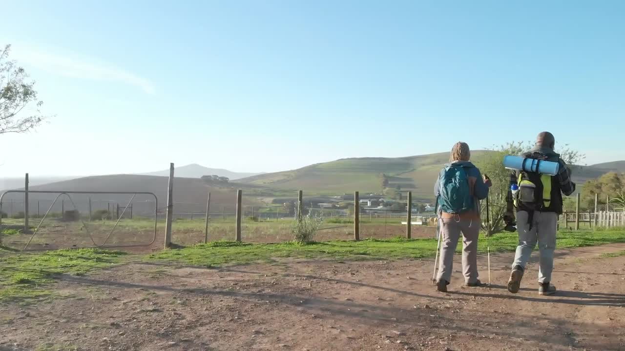 старшая афроамериканская пара с рюкзаками гуляет в солнечной природе с копировальным пространством, замедленным движением