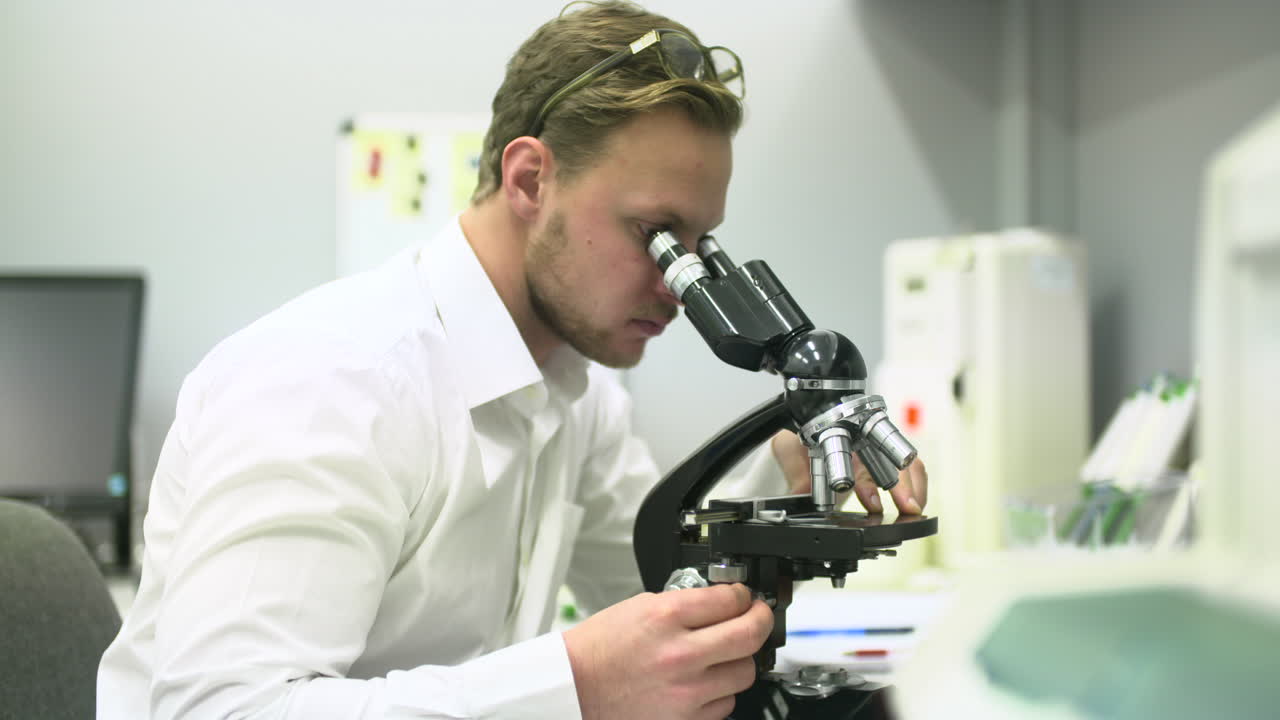 Young Man Examining Samples with a Microscope in a Lab