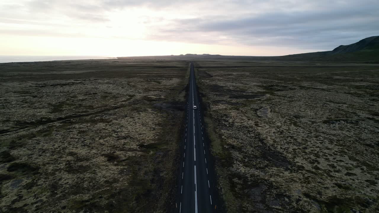 terreno baldío sin fin con una carretera en el medio y un coche todoterreno conduciendo en él, vista aérea