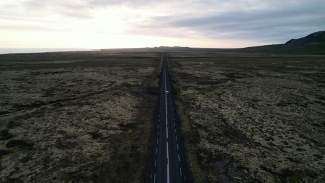 Tierra-Baldía-Sin-Fin-Con-Una-Carretera-En-El-Medio-Y-Un-Coche-Todoterreno-Conduciendo-Por-Ella,-Vista-Aérea