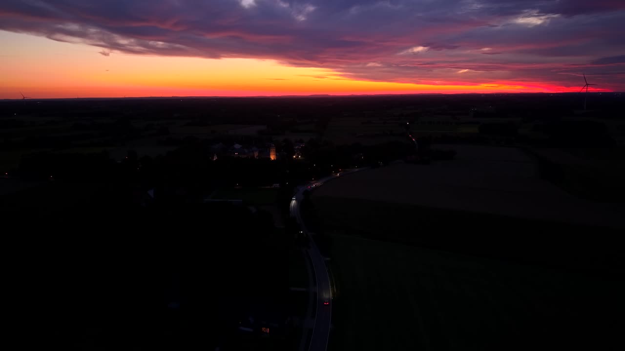 Aerial view of a dramatic sunset with glowing orange and purple sky over a rural landscape, creating a cinematic evening atmosphere. Traffic scene with cars on road. Dusk scene in usa. Wide shot