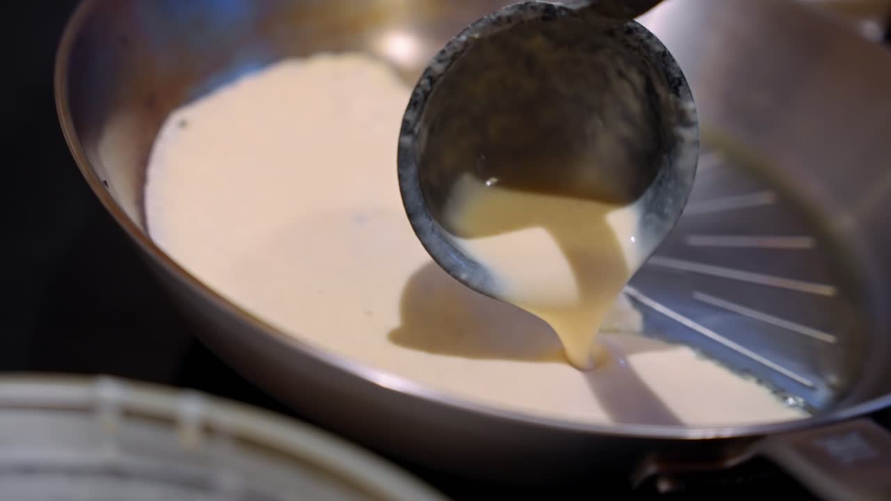 Batter is being poured into a hot frying pan to make pancakes, close-up shot