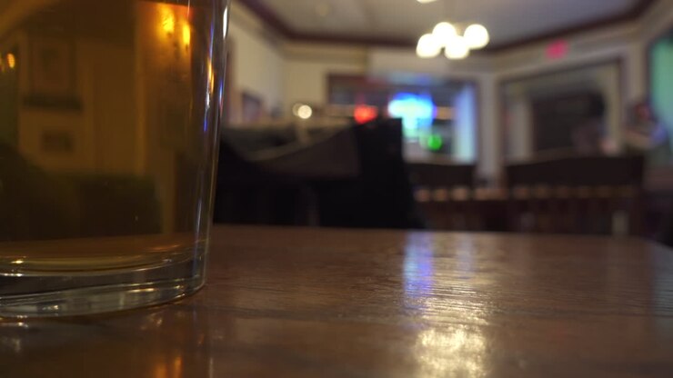 Bicchiere di birra preso e riappoggiato in un bar con diversi avventori che giocano a shuffleboard sfocati sullo sfondo
