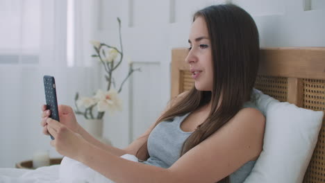 Mujer-Feliz-Haciendo-Videollamada-Usando-Un-Teléfono-Móvil-En-La-Cama.